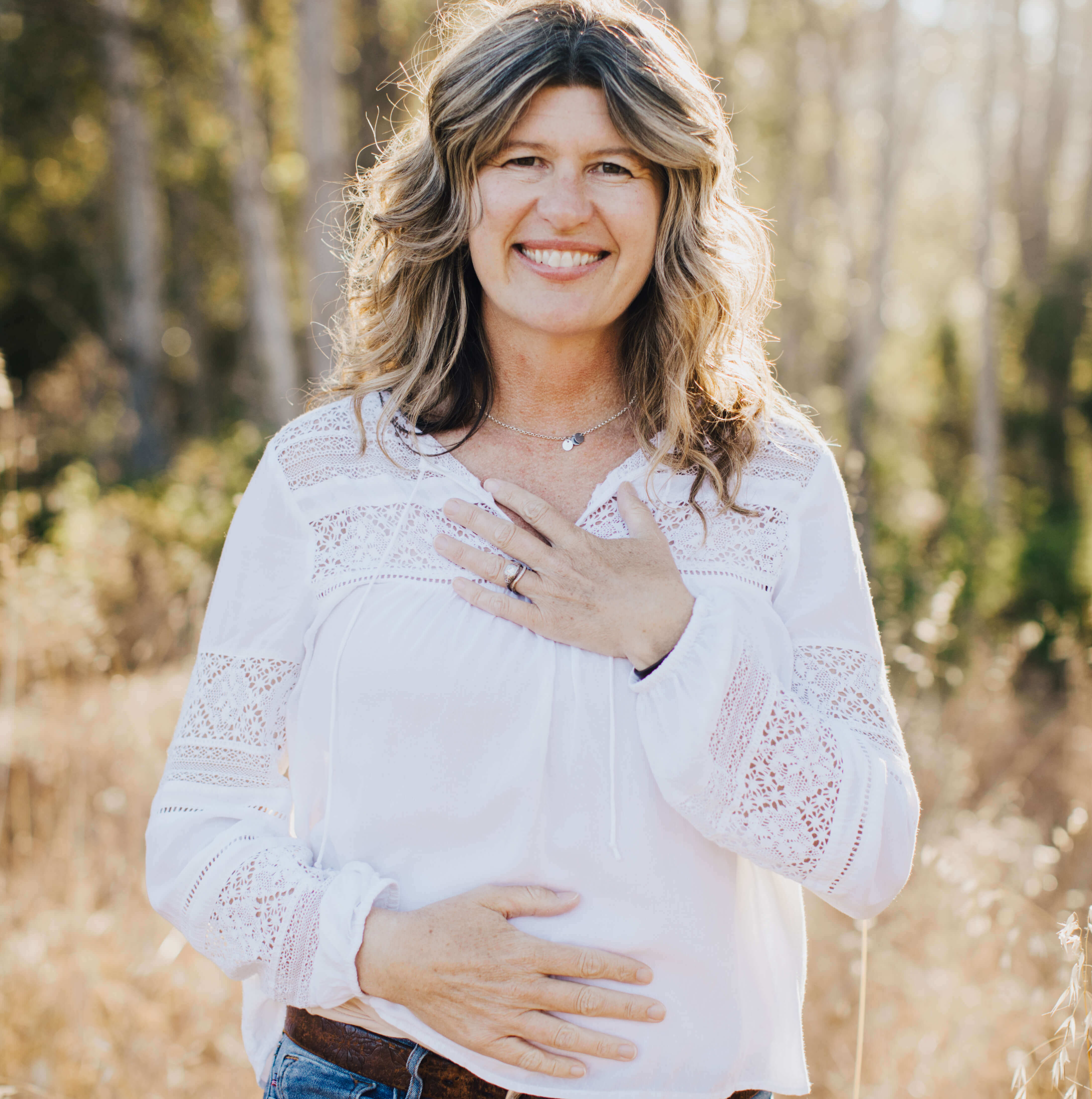 woman smiling with one hand on heart and one hand on belly